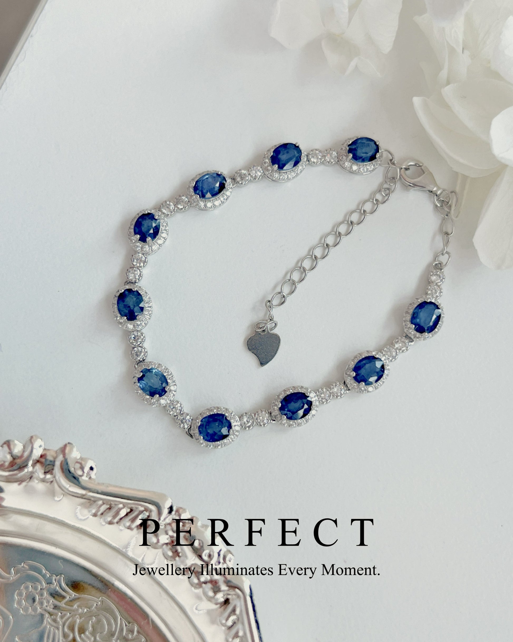 Silver bracelet with blue gemstones on a white surface with flowers.